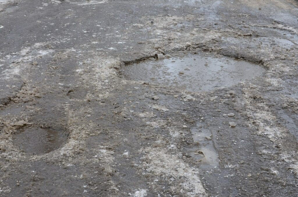 Damaged asphalt road with potholes caused by freezing and thawing cycles during the winter