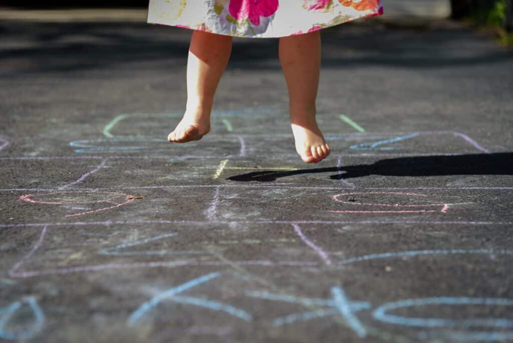 Barefoot little girl playing hopscotch in driveway